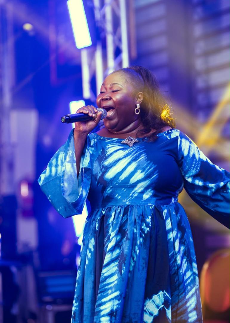 Mercy Sinclear singing joyfully in a blue tie-dye dress on a lit stage