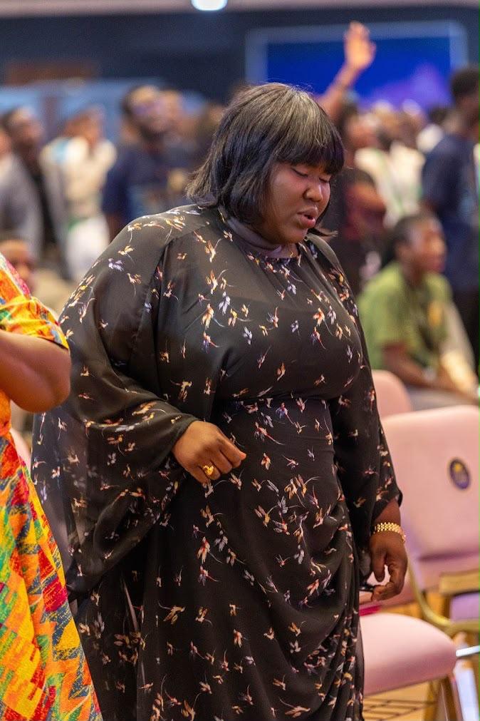 Mercy Sinclear with eyes closed in prayer among a worshipping congregation