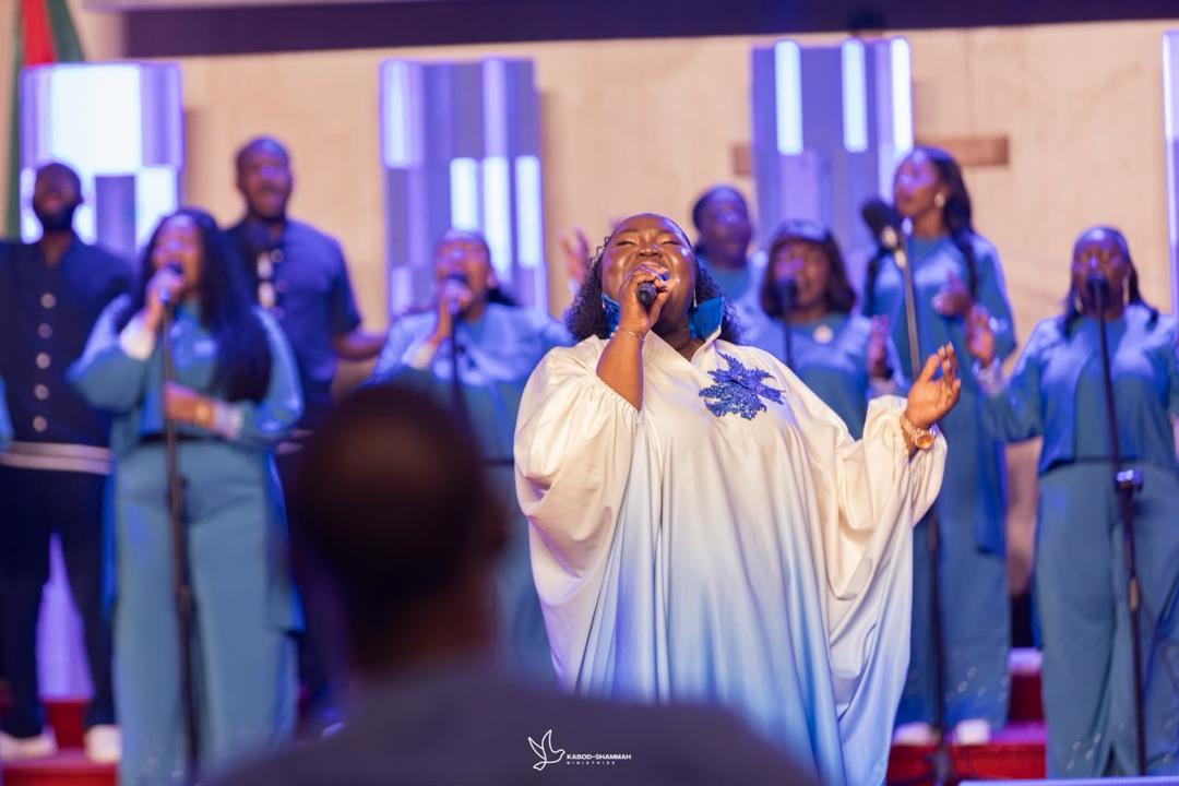 Mercy Sinclear in white leading worship with a choir in blue behind her