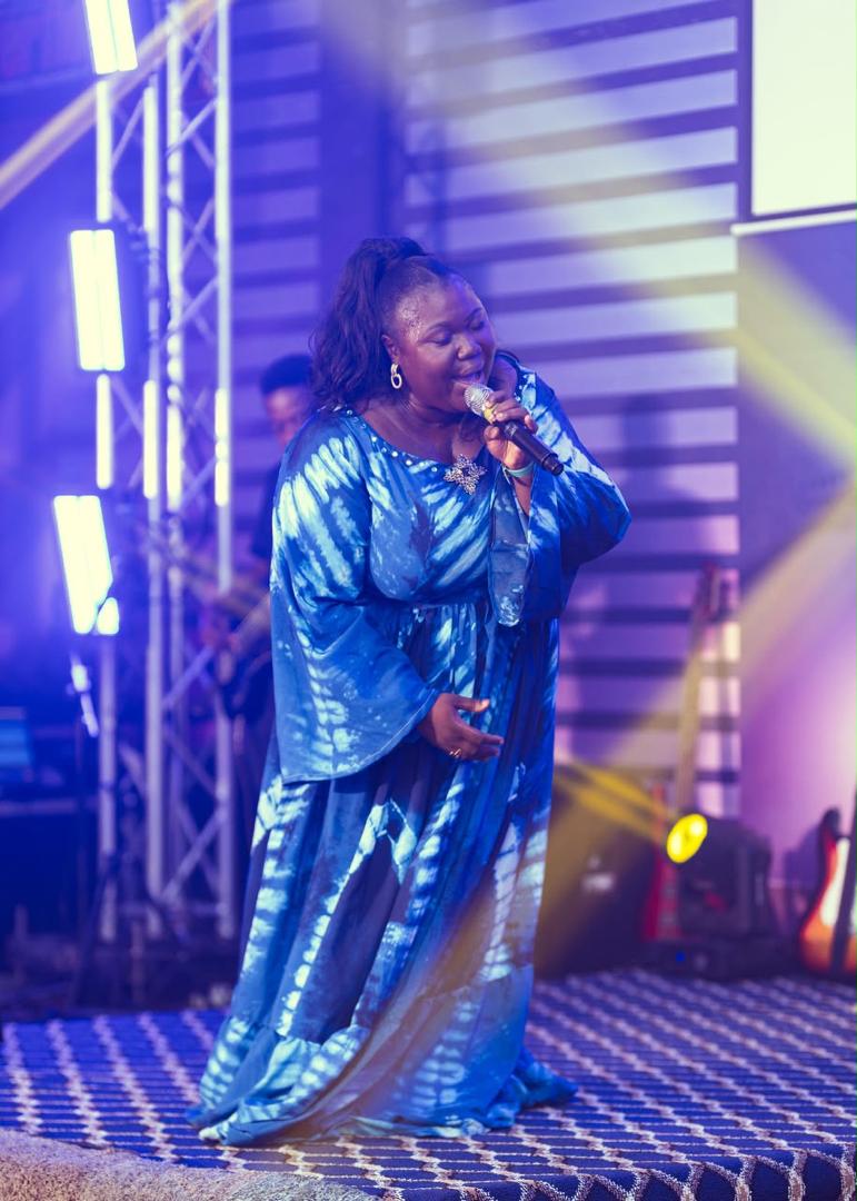 Mercy Sinclear in a blue tie-dye gown singing with eyes closed under purple stage lights