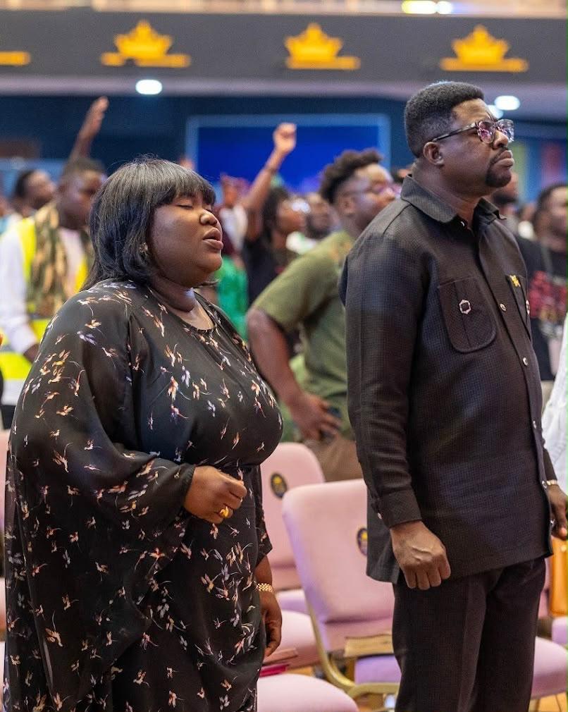 Mercy Sinclear standing with eyes closed in worship beside a man in a congregation