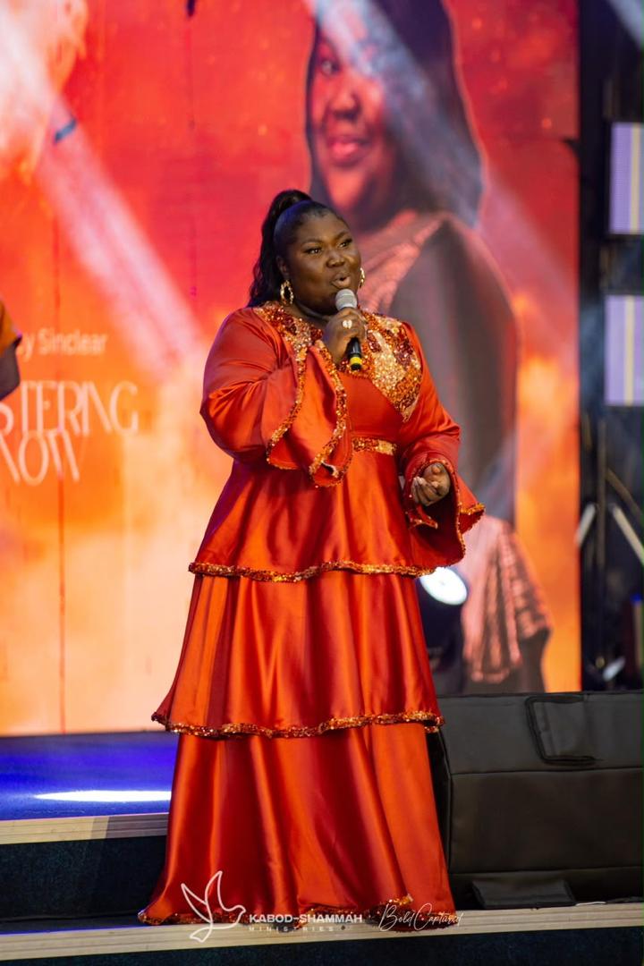 Mercy Sinclear in a tiered orange gown singing on a large stage