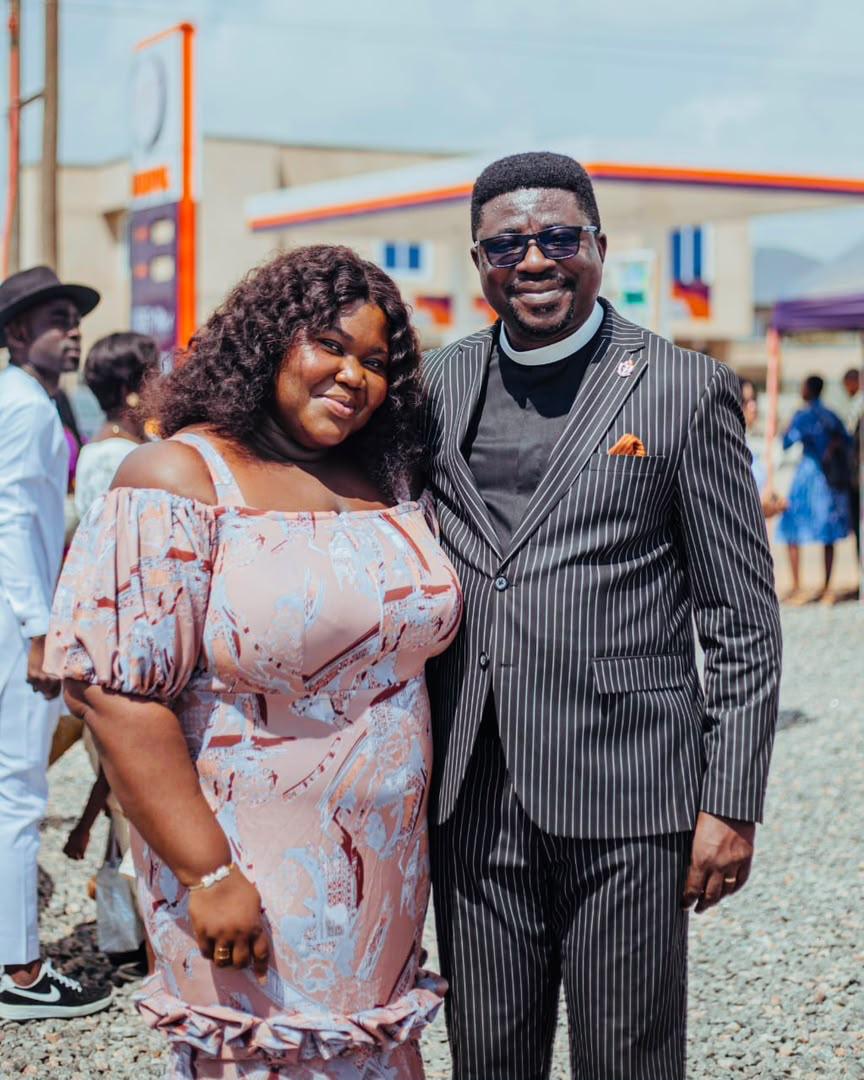 Mercy Sinclear standing beside a gentleman in a pinstripe suit at an outdoor gathering