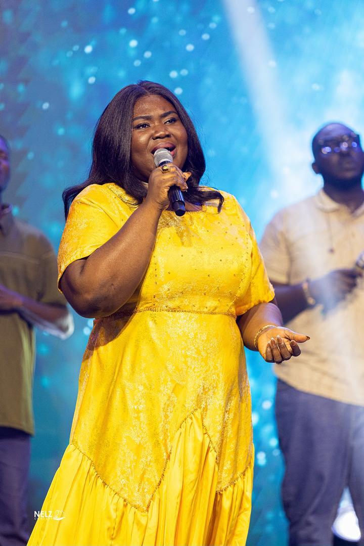 Mercy Sinclear in a yellow dress singing before a blue stage backdrop