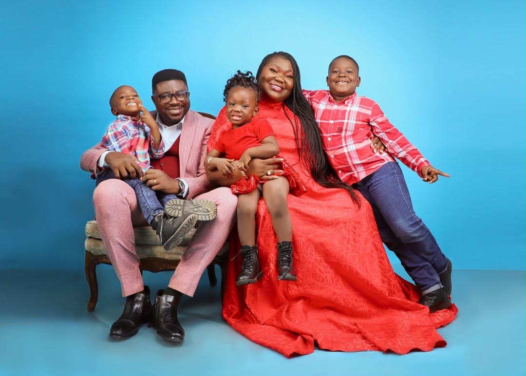 Mercy Sinclear with her husband and children in a studio family portrait against a blue background